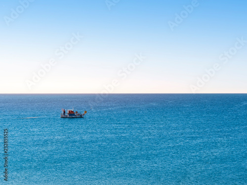 Fisherman fishing by nets in the ocean on a small blue boat on the early morning