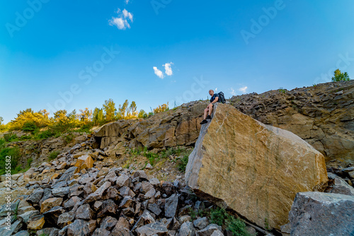 A resting young tourist sitting on the background of the rock and looking straight ahead. Tourism in a warm summer day. © Vadim