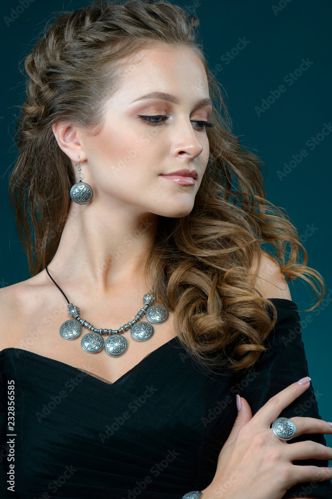 young woman showing off her jewelery in fashion concept wearing accessories and jewelry isolated on blue dark background