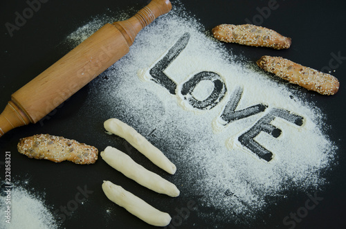 Powdering by flour rolled out dough for bakary stics  with wooden rolling pin over black basground. With love photo