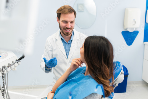 Happy young successful dentist talking to his beautiful female patient about procedures in a modern dental clinic. Teeth whitening and dentistry concept.