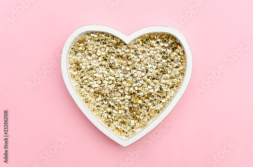 Plate in the shape of a heart filled with gold glitter sequins on a gently pink background. Top view. Love valentines day flat lay