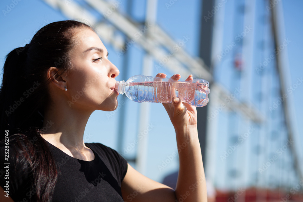 Lovely brunette fit girl drinking water during jogging at the bridge in sunny morning. Space for text Lovely brunette fit girl drinking water during jogging at the bridge in sunny morning. Space for text