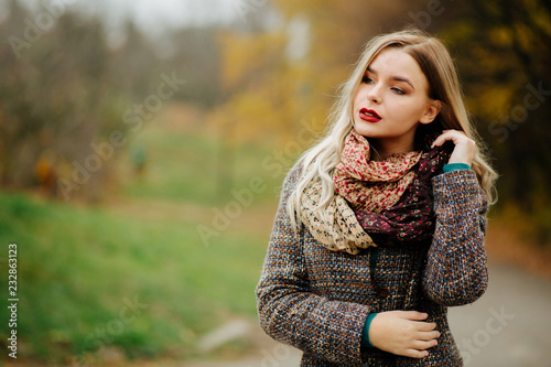 Stylish dressed blonde model with long hair posing at the autumn street. Empty space