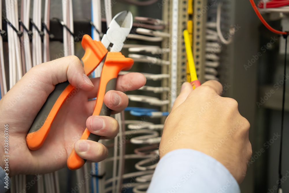 Electric tools in hands of electrician in electrical fuse box.