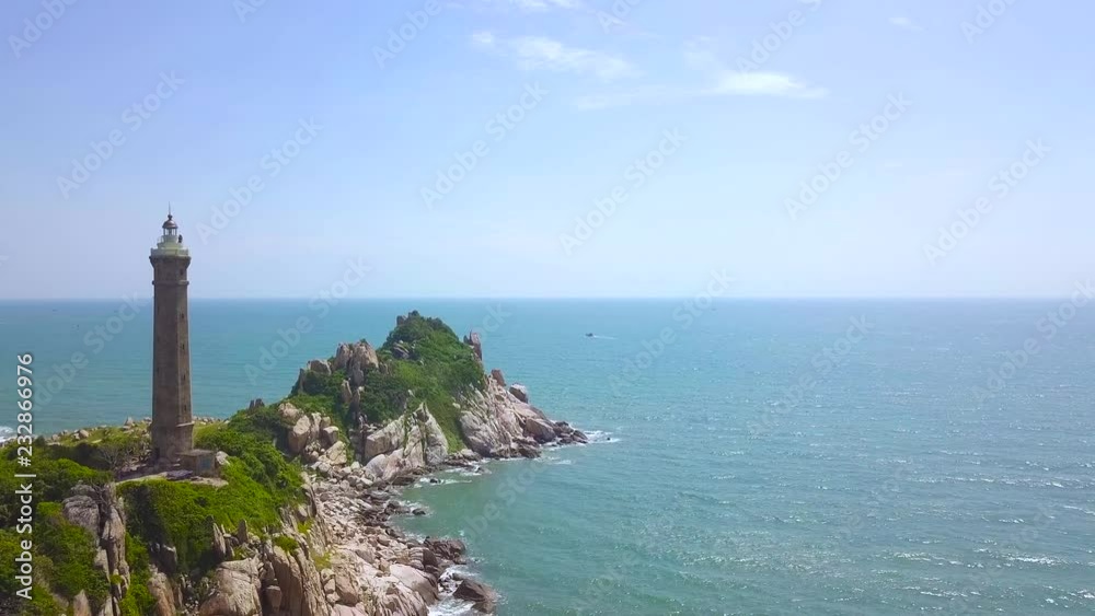 Lighthouse on rocky island in blue sea aerial landscape. Drone view light house on cliff in ocean on blue water and sky background. Lighthouse on rocky island in blue sea aerial landscape. Drone view light house on cliff in ocean on blue water and sky background.