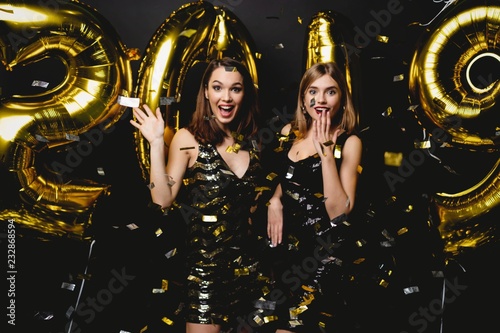 Beautiful Women Celebrating New Year. Happy Gorgeous Girls In Stylish Sexy Party Dresses Holding Gold 2019 Balloons, Having Fun At New Year's Eve Party. Holiday Celebration. High Quality Image