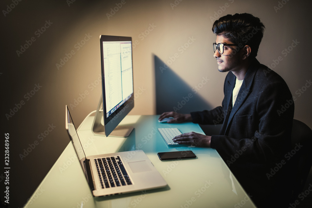 Indian young man sitting and using blank screen computer in dark room Indian young man sitting and using blank screen computer in dark room