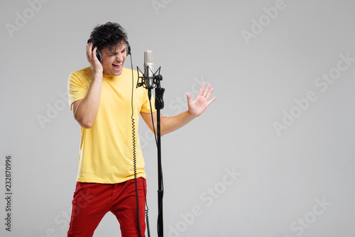 Portrait of handsome man in headphones sing on studio microphone on grey background. Singer concept.