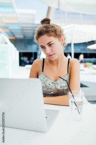 Beautiful young woman sitting outdoors and chatting, drinking cocktail using laptop a in cafe.
