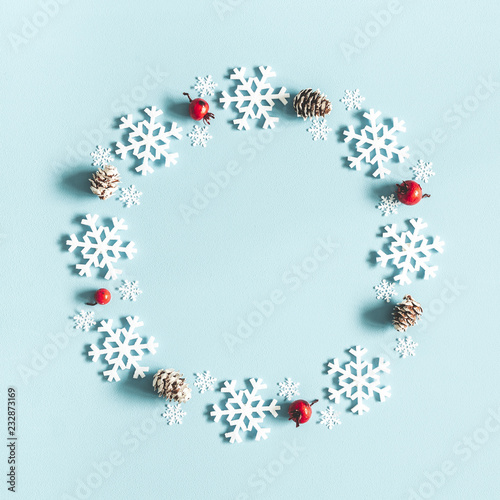 Christmas or winter composition. Wreath made of snowflakes, pine cones and red berries on pastel blue background. Christmas, winter, new year concept. Flat lay, top view, copy space