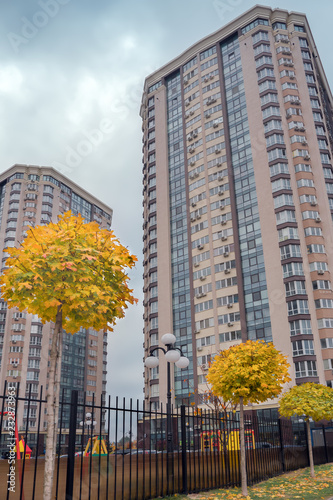 Modern apartment building with a neat adjoining territory and a luscious yellow trees. Residential apartment building on the background of the autumn. Skyscraper with playground territory.
