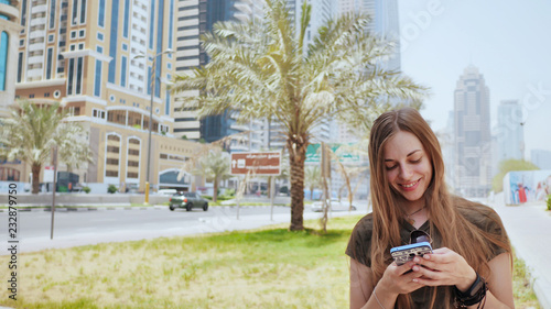 Photography The girl dials a number or message on the smartphone against the backdrop of the city streets of Dubai