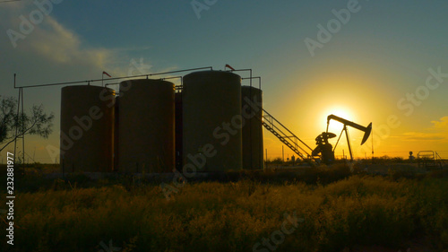 Industrial jack pump platform pumping crude oil against sunset sun
