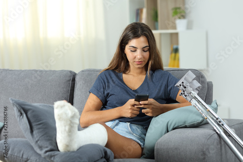 Fotografie Disabled woman texting on phone on a couch at home