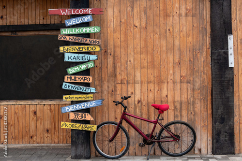 Red Bike Next to a Post with Welcome Signs in Several Different Languages.  English, Afrikaans, German, Xhosa, Spanish, Swahili, Portuguese, Oshiwambo, Italian, Russian, French, Japanese, Korean photo
