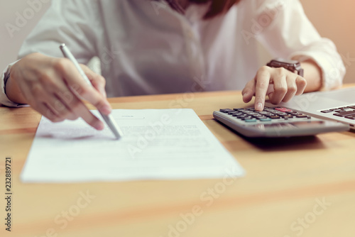 woman check agreement documents and using calculator on table in office room, to plan advance budget.