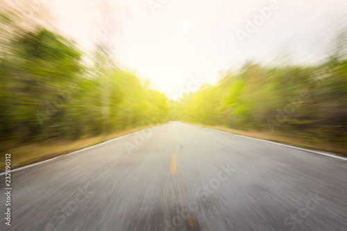 View of the empty asphalt road along the forest in motion blur with beautiful yellow lighting background.