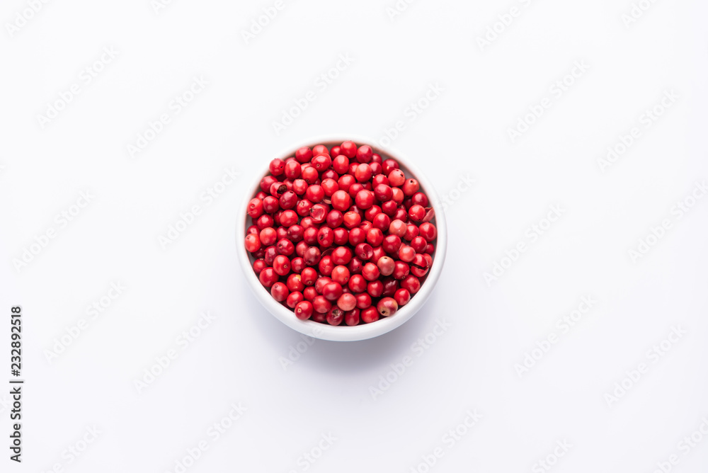 White bowl of Pink Pepper, Brazil Pepper, Rose pepper, Schinus terebinthifolius seeds over white background, top view