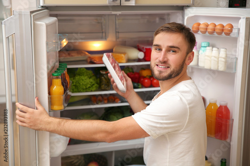 Young man taking meat from refrigerator in kitchen