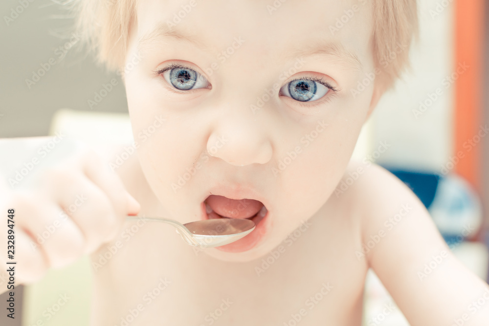Cute child with blue eyes drinking tea from a spoon in the kitchen. Cute child with blue eyes drinking tea from a spoon in the kitchen.