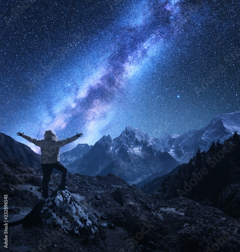 Silhouette of a standing man with raised up arms on the stone  mountains and starry sky with Milky Way at night in Nepal. Sky with stars. Travel. landscape with mountain ridge and milky way. Space