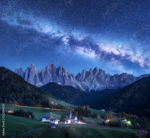 Santa Maddalena and Milky Way at night in autumn in Italy. Starry sky with milky way over St. Magdalena and mountains. Village with houses, church, green meadows, trees, rocks. Val di Funes. Space