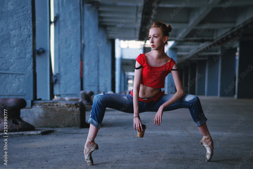 Ballerina dancing with a cup of coffee in jeans, t-shirt and pointe. Street performance. Modern ballet. Slim girl holding a paper glass with a hot drink.