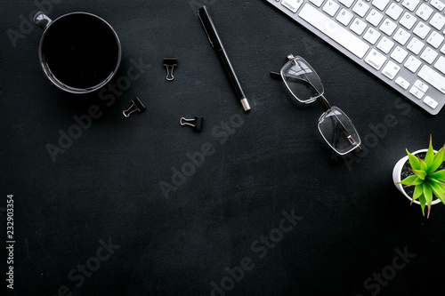 Flat lay of office desk, office workplace. Keyboard and glasses near coffee and stationery on black background top view copy space