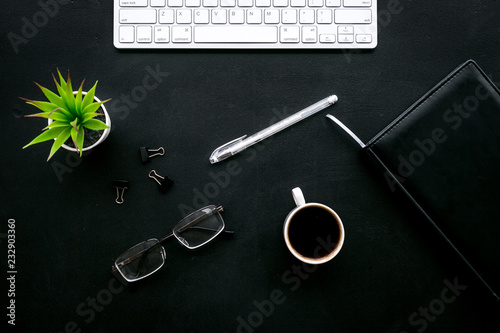 Flat lay of office desk, office workplace. Keyboard and glasses near coffee and stationery on black background top view