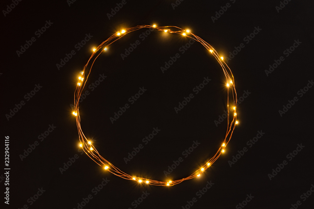Christmas lights garland circular border over black background. Flat lay, copy space.