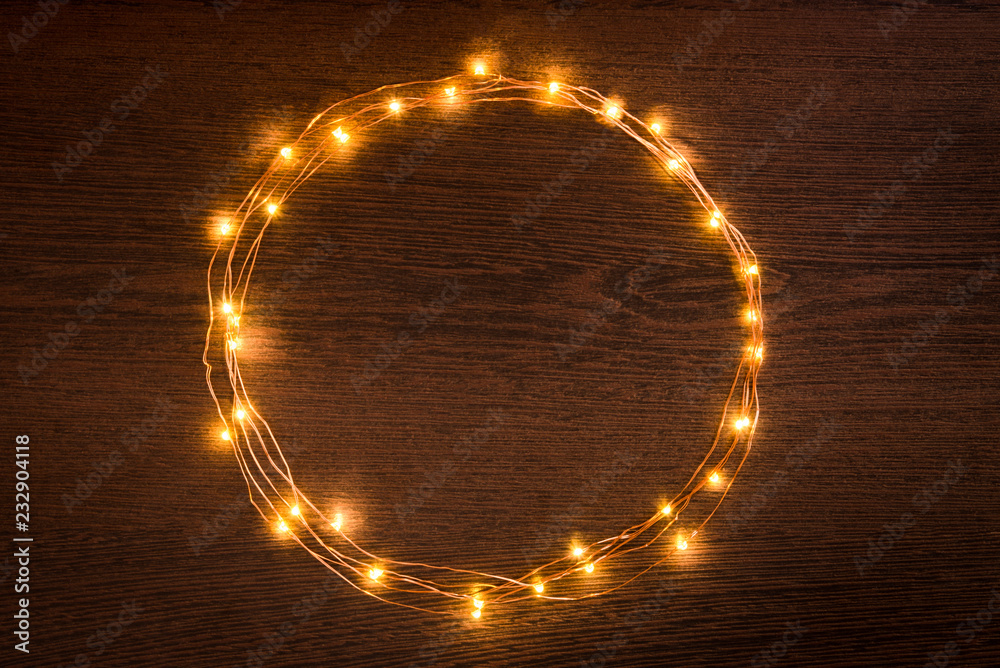 Christmas lights garland circular border over dark wooden background. Flat lay, copy space.