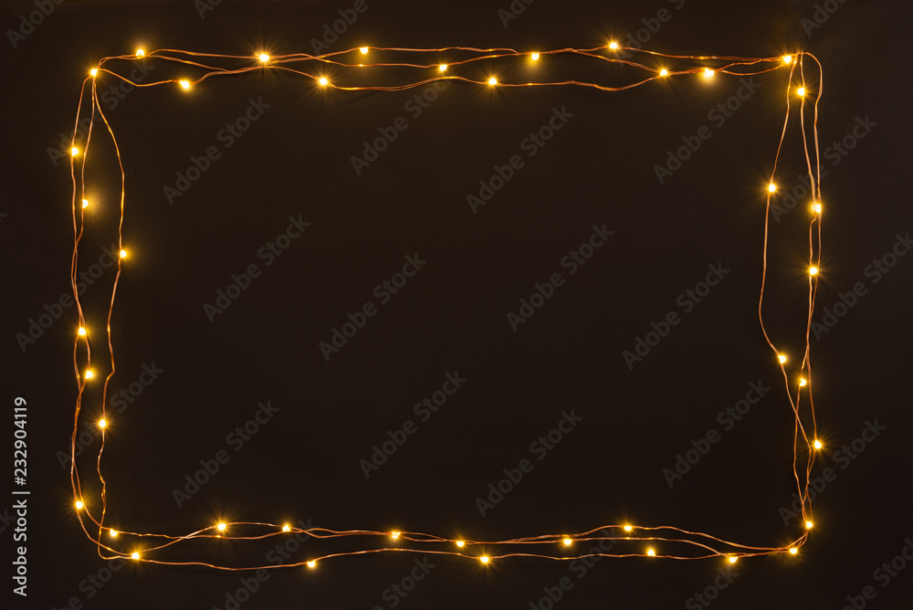 Christmas lights garland border over black background. Flat lay, copy space.