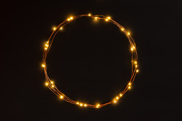 Christmas lights garland circular border over black background. Flat lay, copy space.