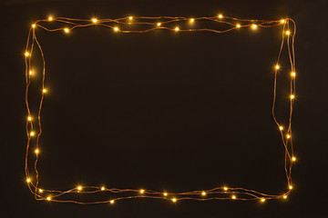Christmas lights garland border over black background. Flat lay, copy space.