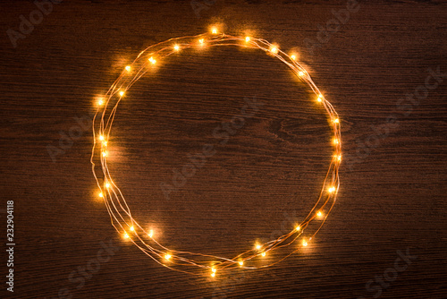 Obraz na płótnie Christmas lights garland circular border over dark wooden background. Flat lay, copy space. w salonie