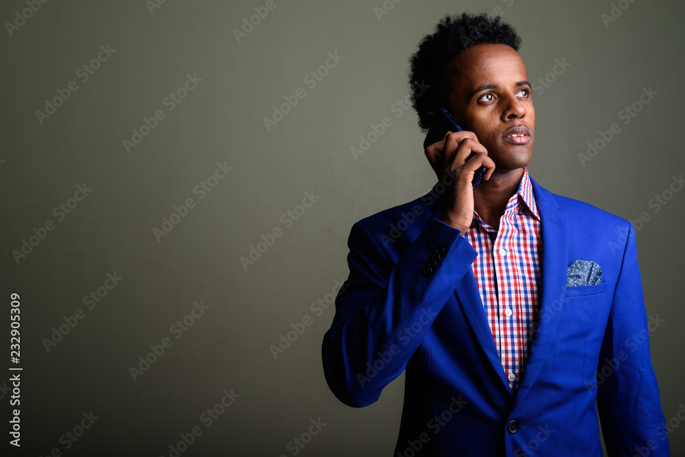 Young handsome African businessman using mobile phone against co Young handsome African businessman using mobile phone against co