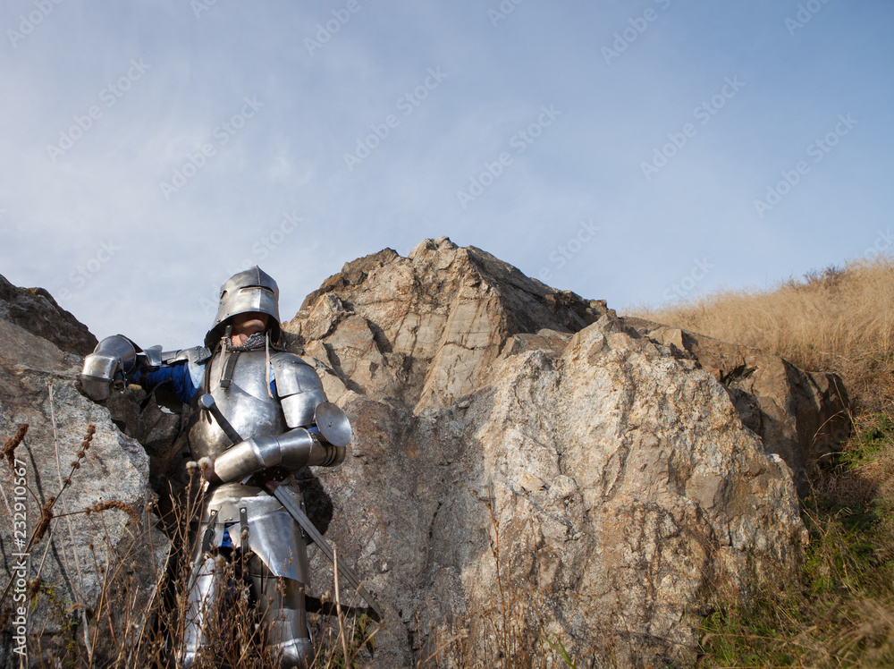 Knight with a sword and in medieval armor on the background of granite stone Knight with a sword and in medieval armor on the background of granite stone