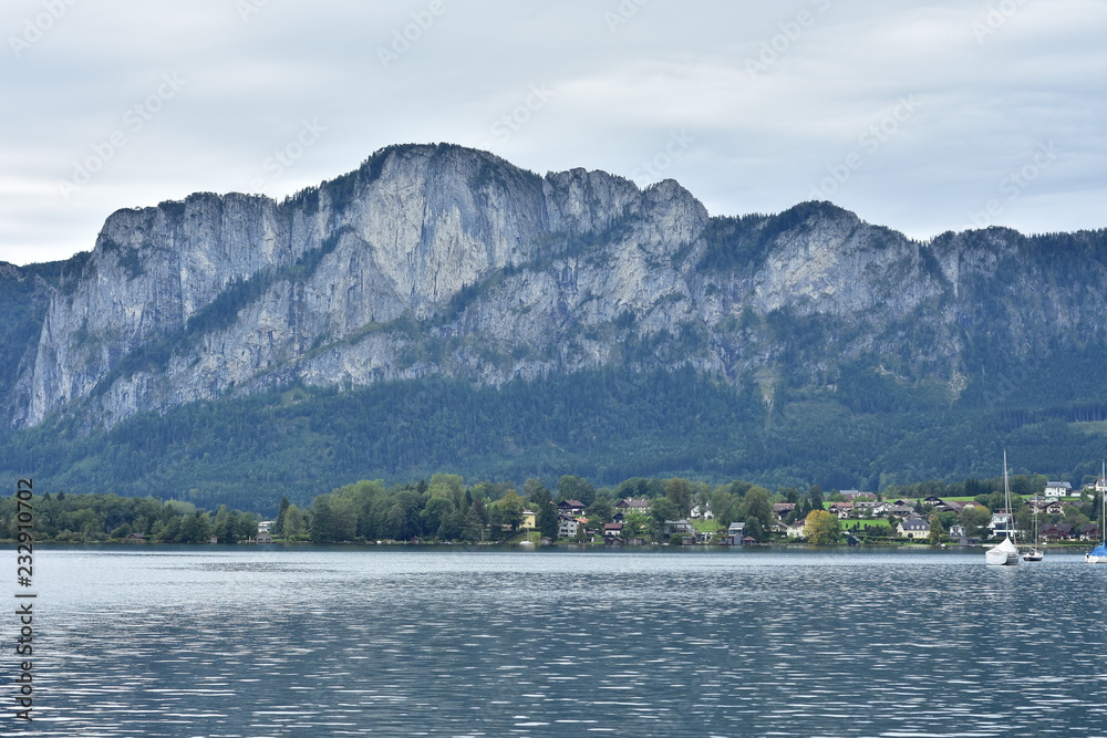 Calm surface of Attersee lake reflecting light with mountains in background on cloudy day. Calm surface of Attersee lake reflecting light with mountains in background on cloudy day.