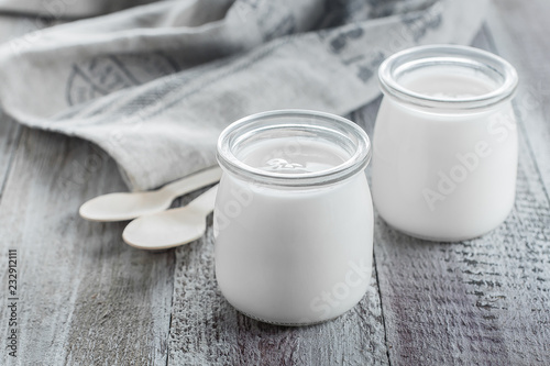 Greek yogurt in a glass jars with wooden spoons on wooden background. Healhty Breakfast Food. Copy space photo