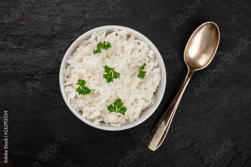 A bowl of cooked white long rice, shot from above on a black background with a spoon and a place for text