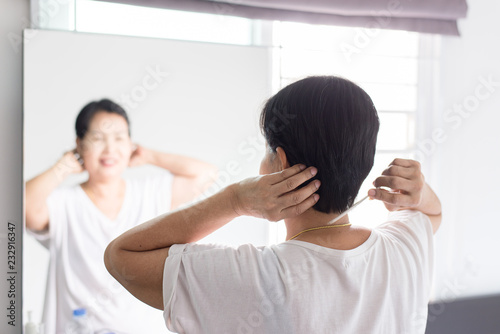 Elderly woman using comb with her hair in front of mirror,Back view