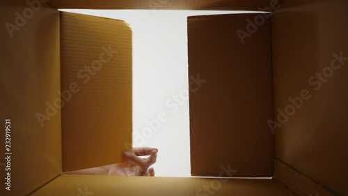 Happy young man opens a cardboard box after moving home and is looking for product inside the box