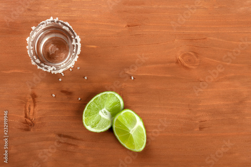 A photo of a tequila shot with lime wedges, shot from above on a rustic background with a place for text