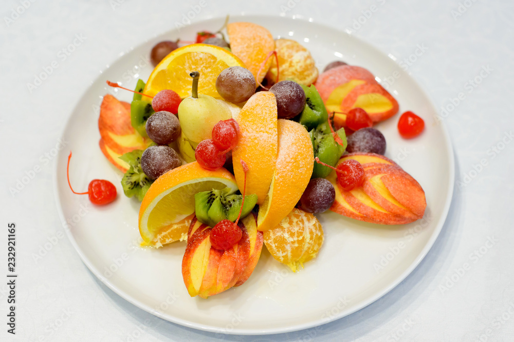 Sweet fresh fruits on white plate. Orange, apple, grapes, pear, kiwi, cherry. Healthy food style