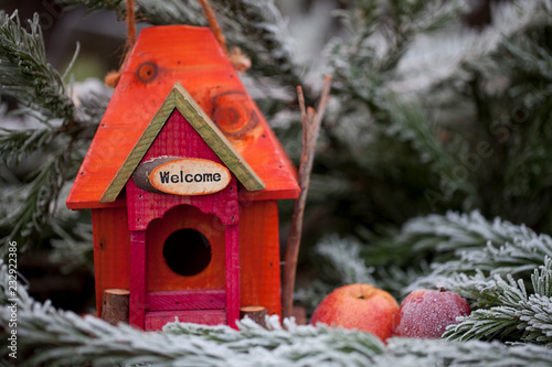 cute red and orange bird house with welcome sign, apples and frosty fir branches