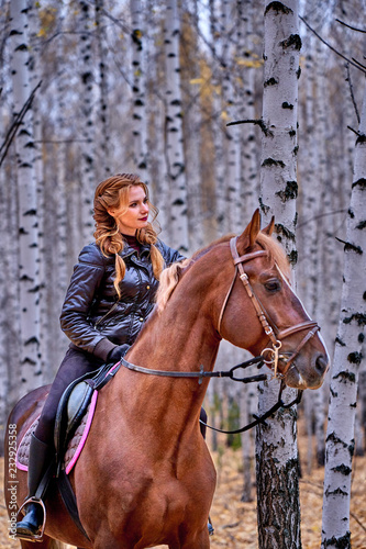 Portrait of a young beautiful woman with long brown hair. Woman on a horse walk in the forest. © afefelov68