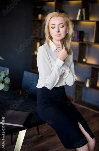 Young beautiful business lady in a white blouse sitting on the table in the office. Business concept. Sexy business lady