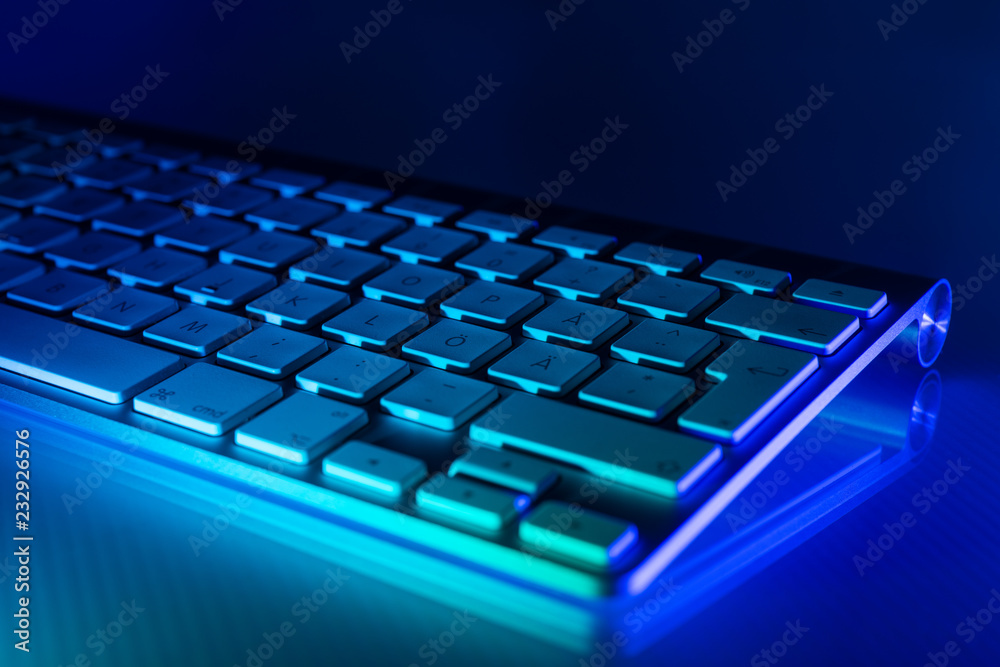Aluminum keyboard illuminated in blue and turquoise with mirroring on glass Aluminum keyboard illuminated in blue and turquoise with mirroring on glass