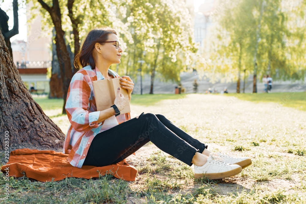 Beautiful mature woman with glasses reading book sitting on the grass near the tree in the park at sunset. Beautiful mature woman with glasses reading book sitting on the grass near the tree in the park at sunset.